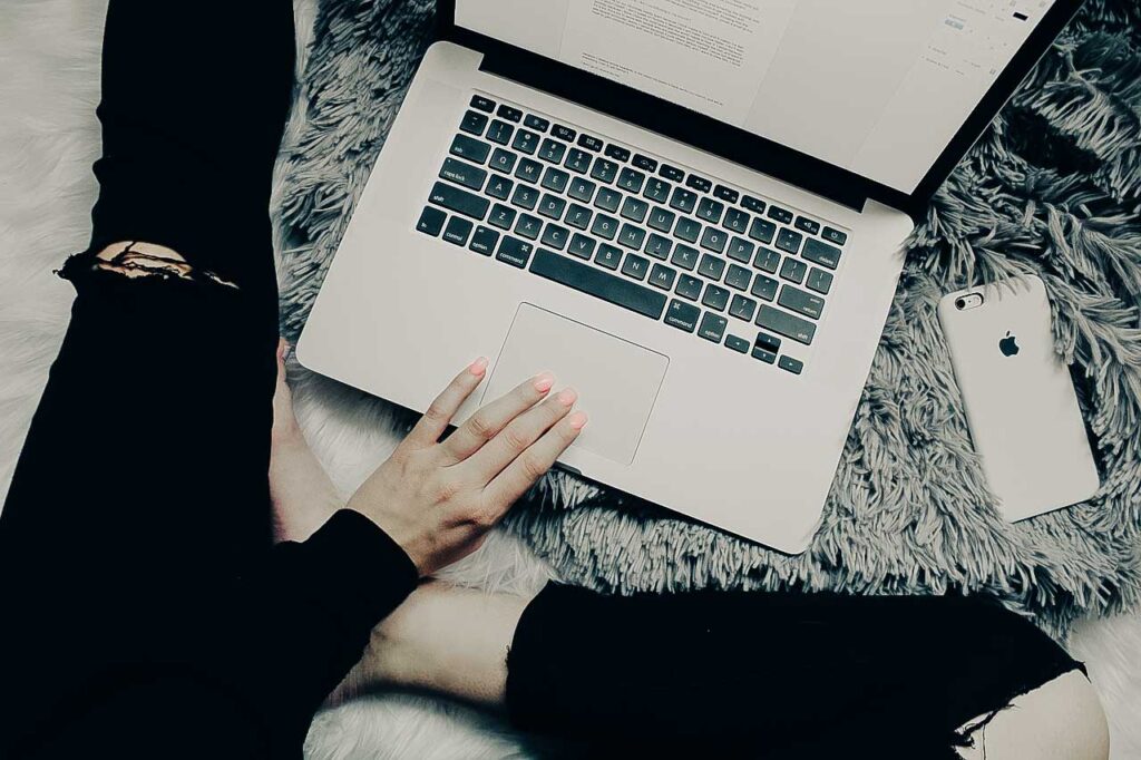 Woman working on laptop with iPhone nearby.