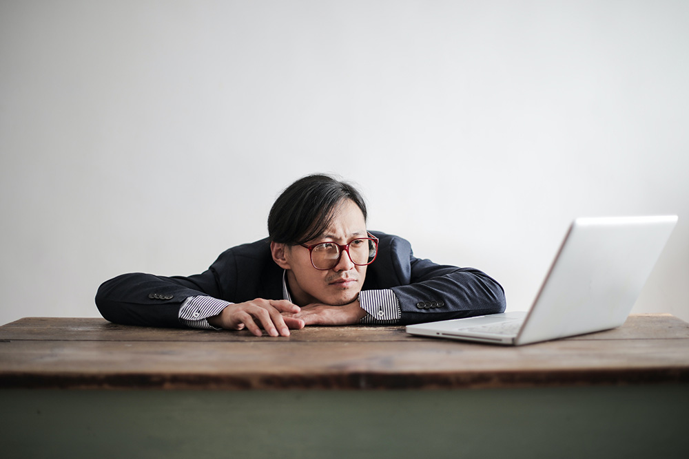 Businessman looking tired at laptop on desk.