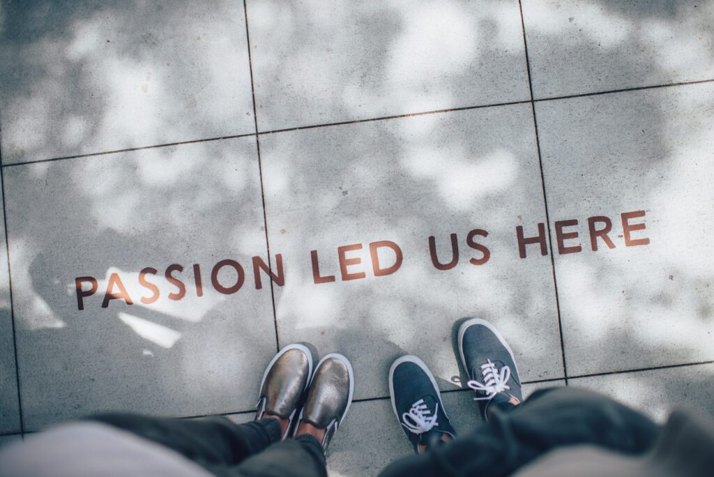 Feet beside 'Passion Led Us Here' pavement inscription.