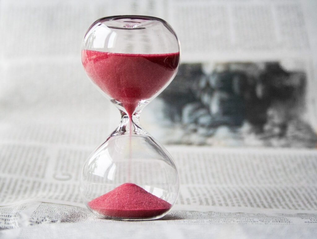 Hourglass with red sand on newspaper background.