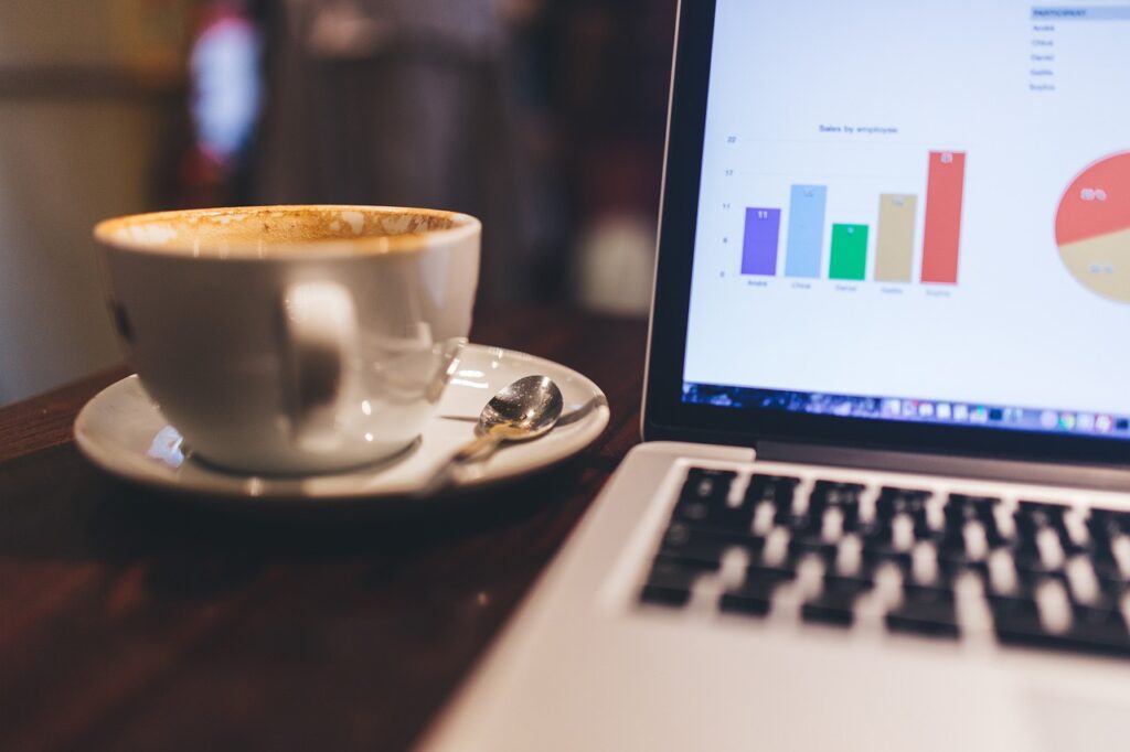 Empty coffee cup beside laptop displaying graphs.