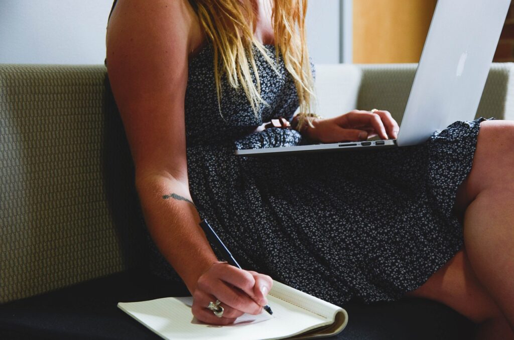 Woman working on laptop with notepad.