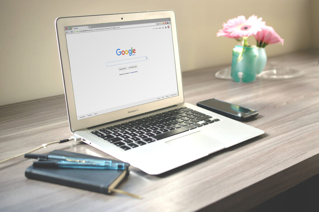 Laptop with Google search, phone, pens, and pink flowers.