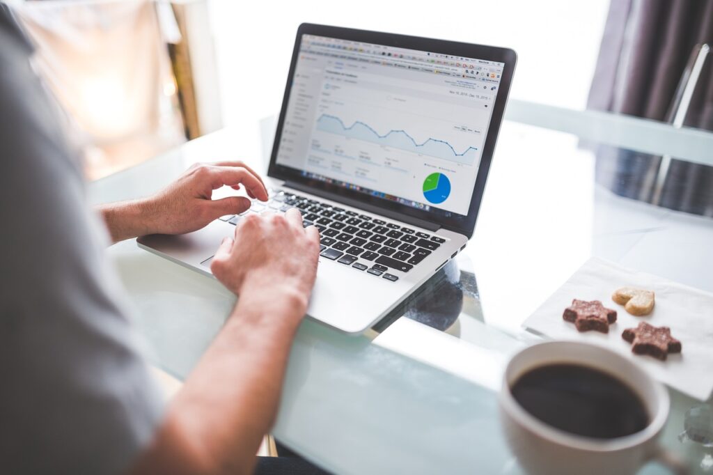 Person analyzing data on laptop with coffee and snacks.