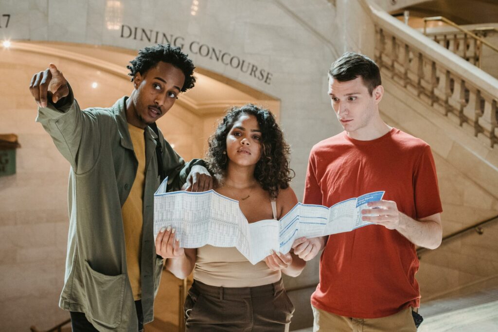 Three friends consulting map indoors, pointing and discussing.