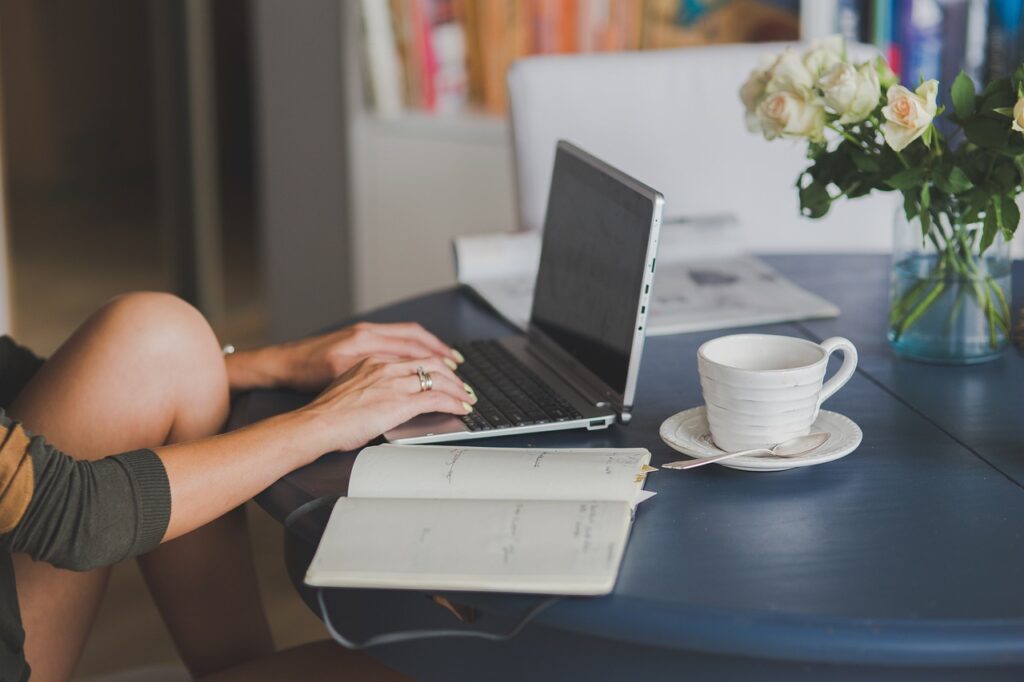 Woman working on laptop with coffee and notebook.