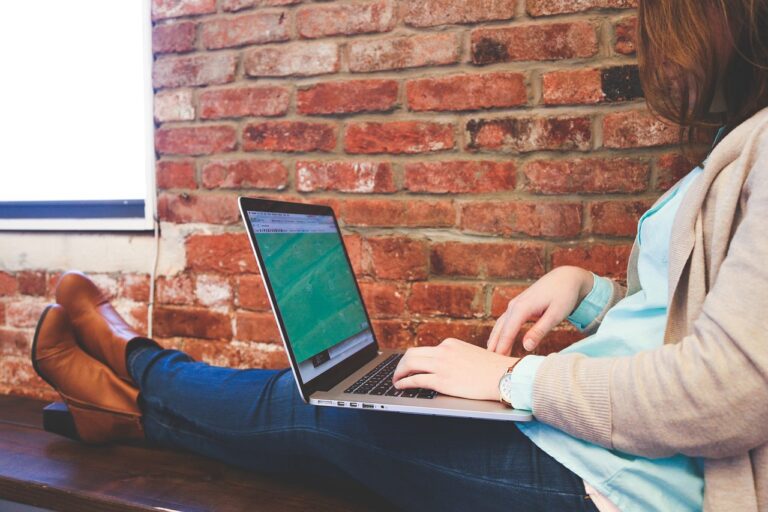 Person working on laptop against brick wall.