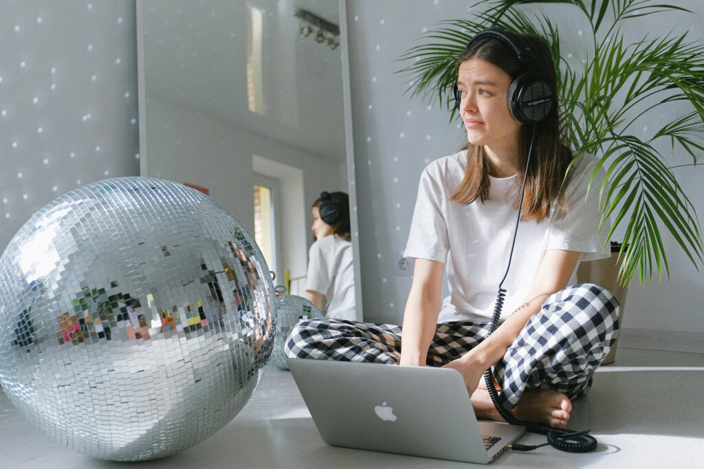 Woman with headphones on laptop beside disco ball.