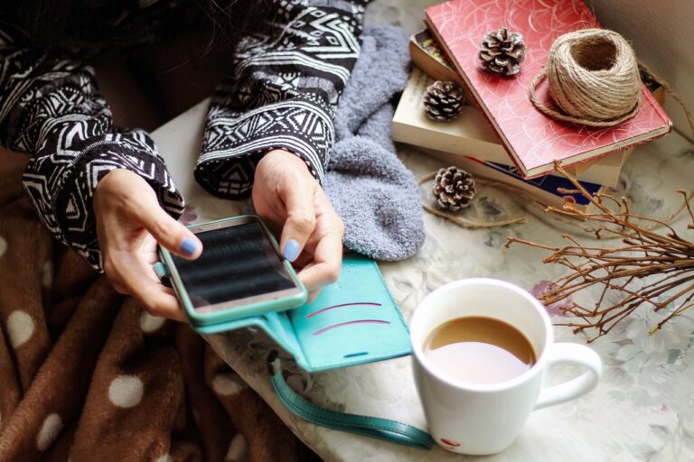 Person holding phone with coffee and books nearby.