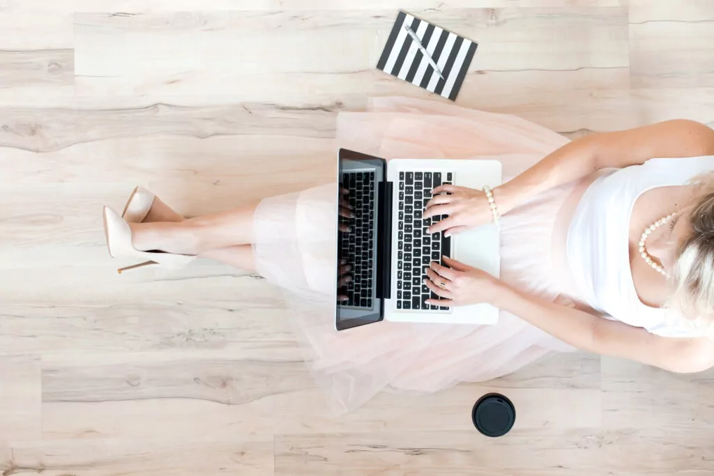 Woman in white dress using laptop on wooden floor