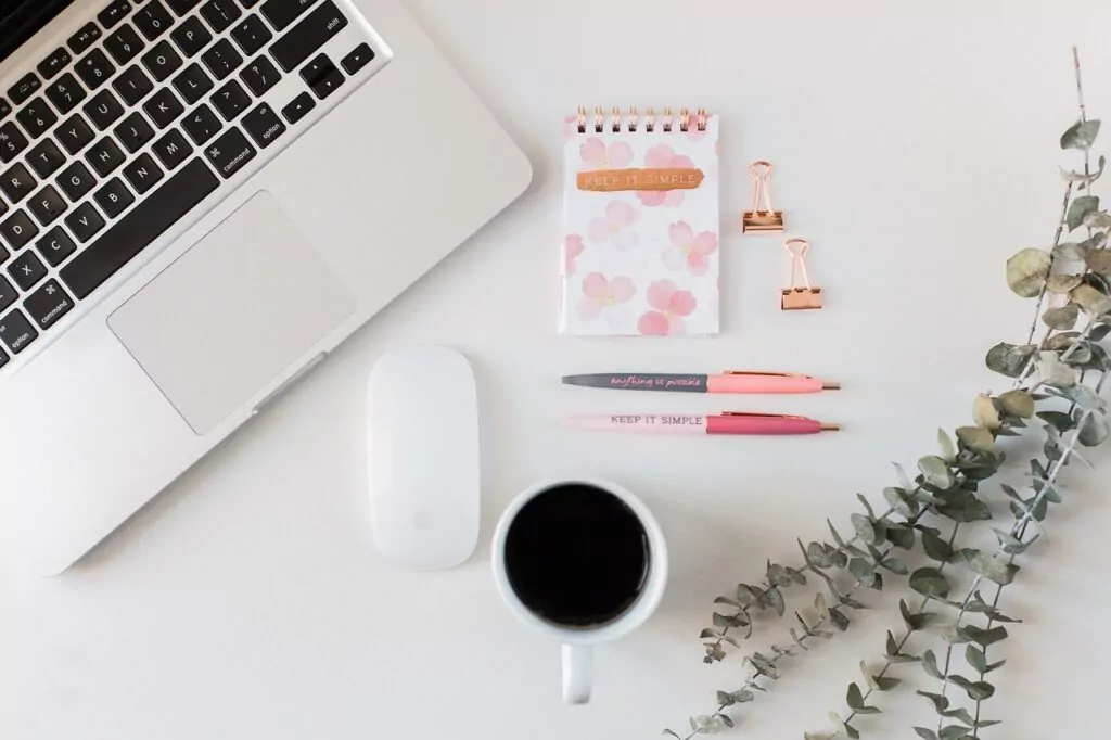 Minimalist workspace with laptop, notepad, pens, and coffee.