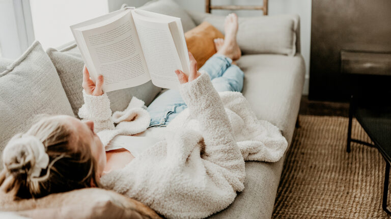 Woman reading book on cozy sofa with bare feet up