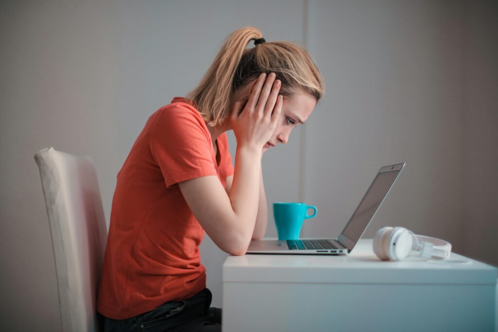 Stressed woman using laptop with coffee and headphones