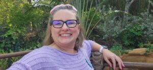 Smiling woman with glasses in a lush garden setting