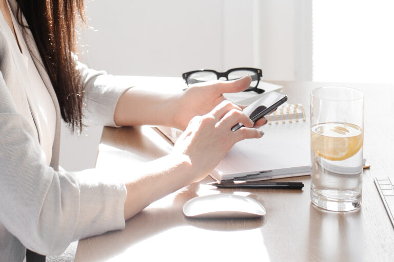 Professional woman working at desk with smartphone and notepad