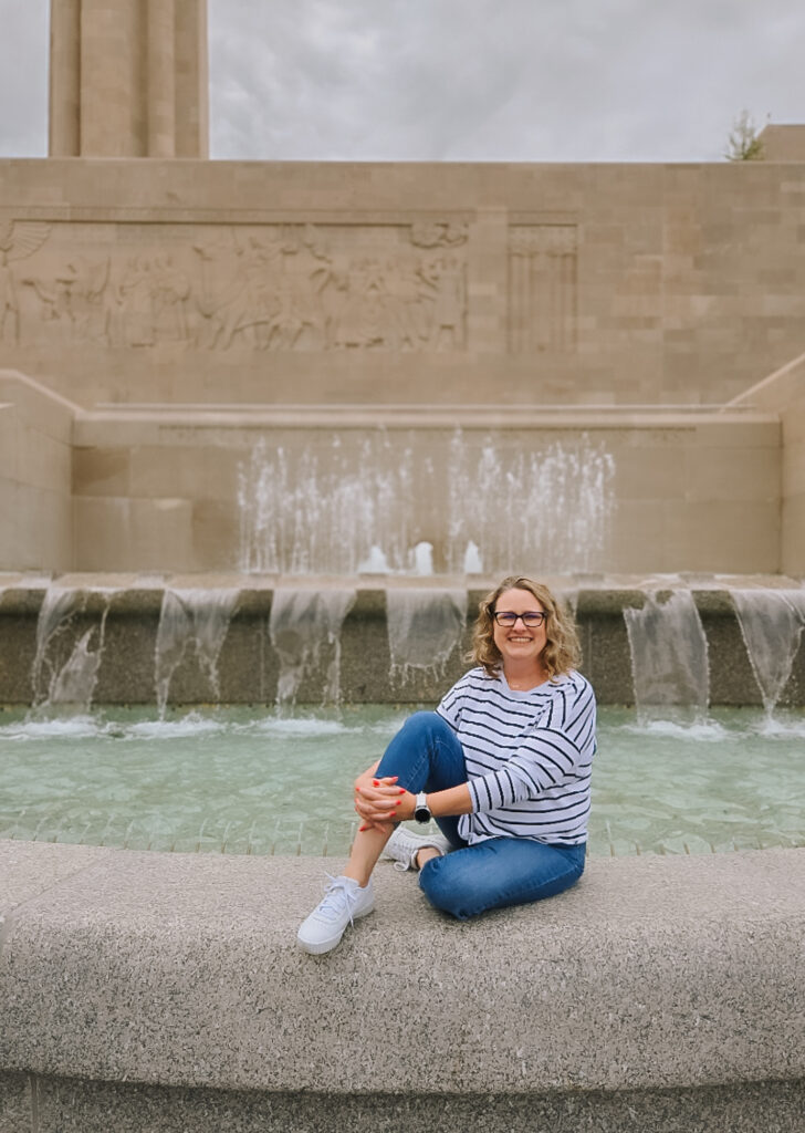 Smiling person sitting by a fountain at a monument.