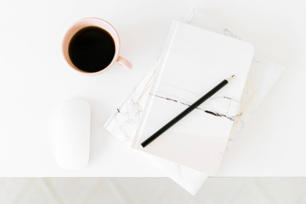 Coffee, notebook, pencil, and mouse on white desk.