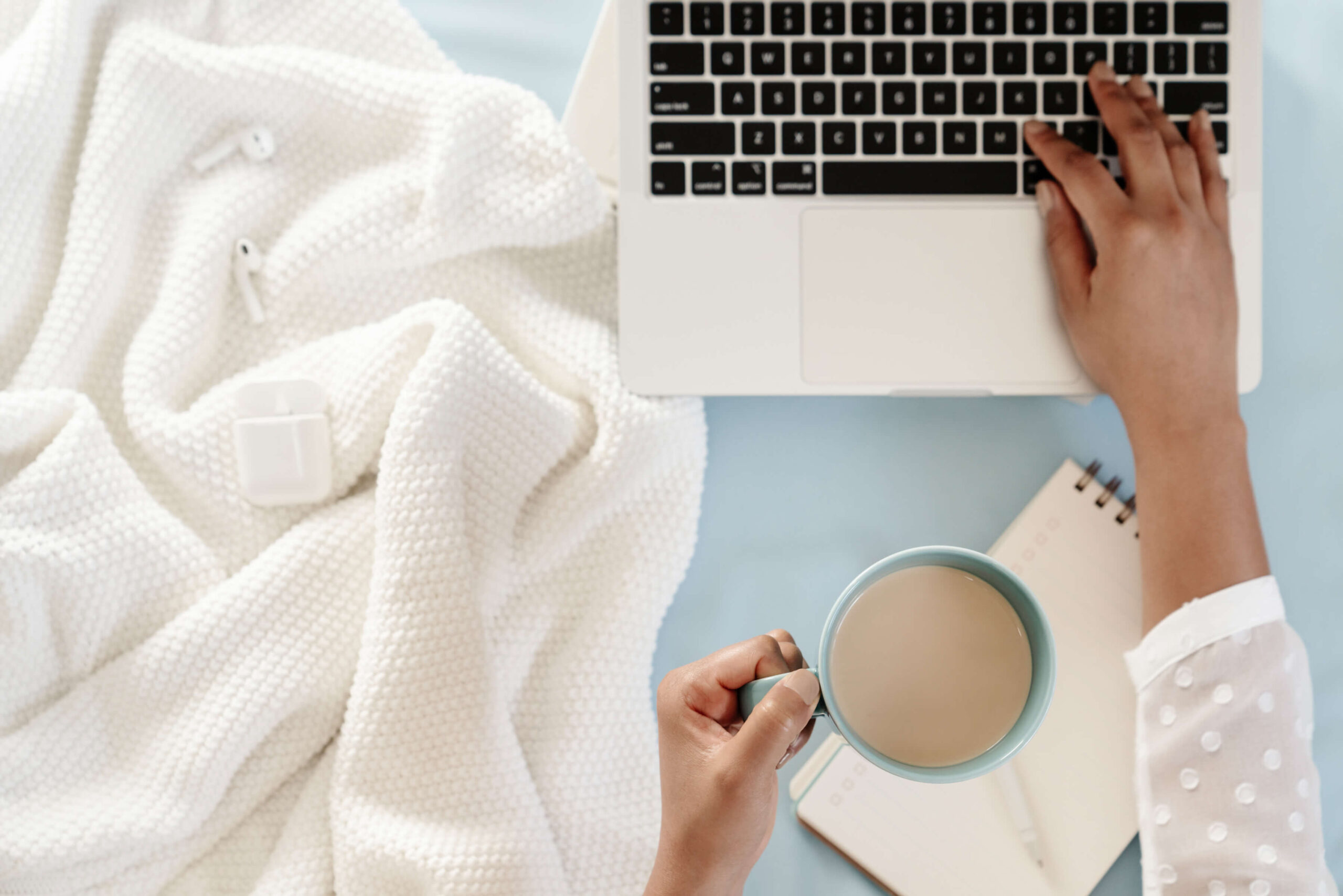 Person working on laptop with coffee and blanket.