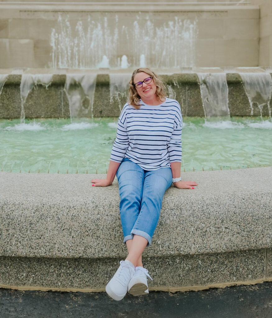 Person smiling by a fountain in casual attire.