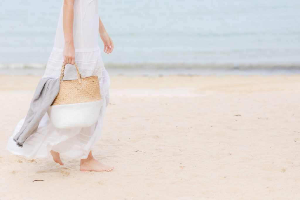 Woman walking on beach with straw bag