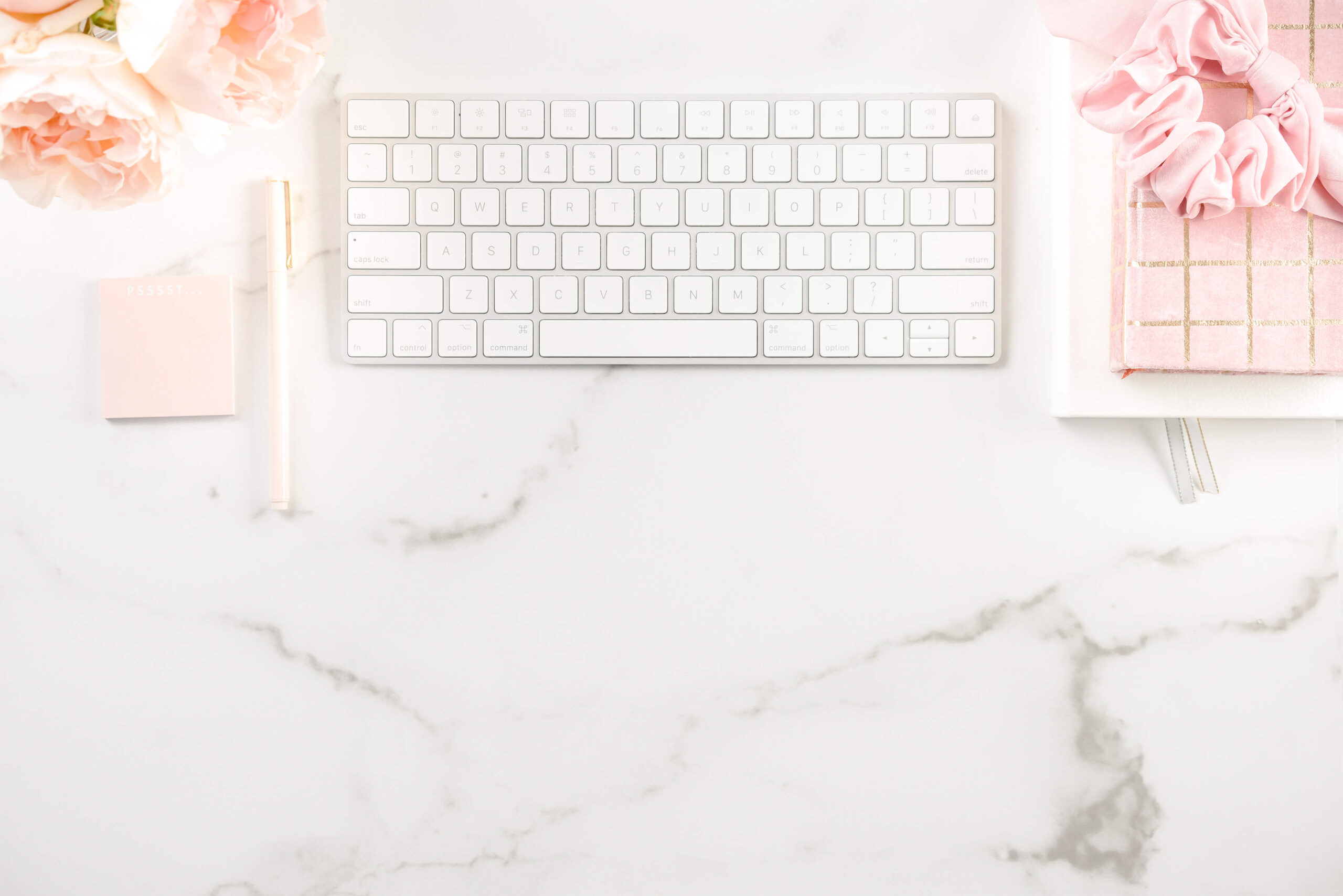 Marble desk with keyboard, pen, and pink notepad.