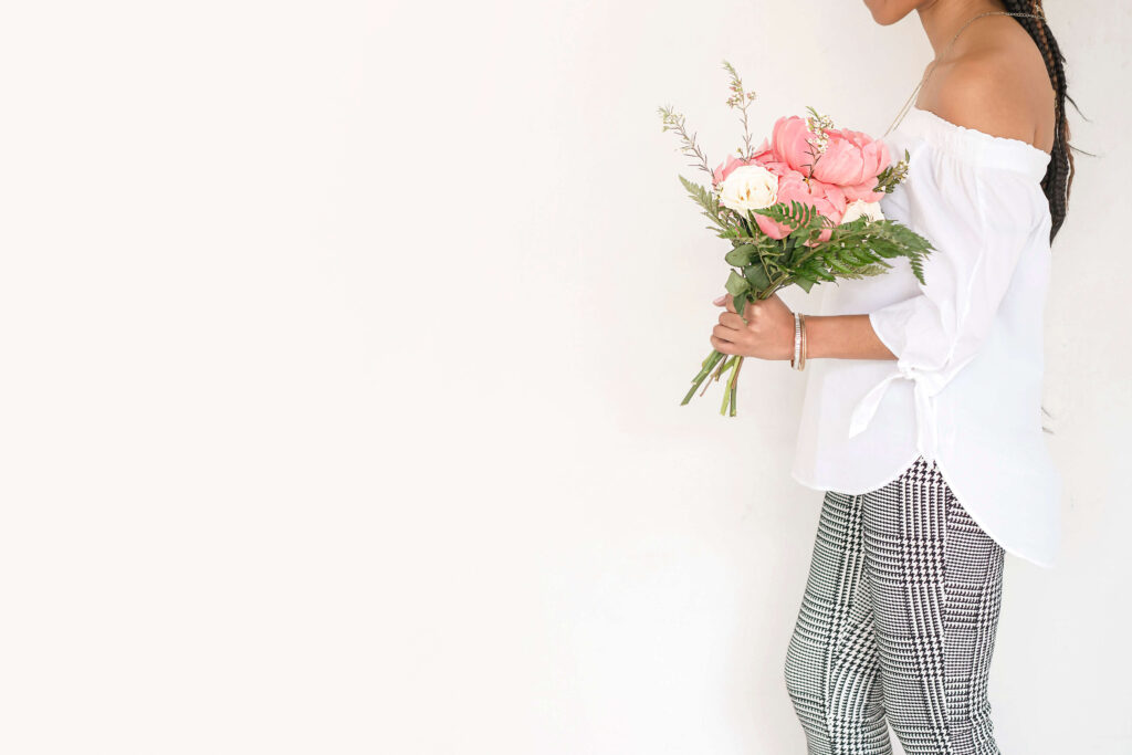 Woman holding bouquet wearing white top and plaid pants.