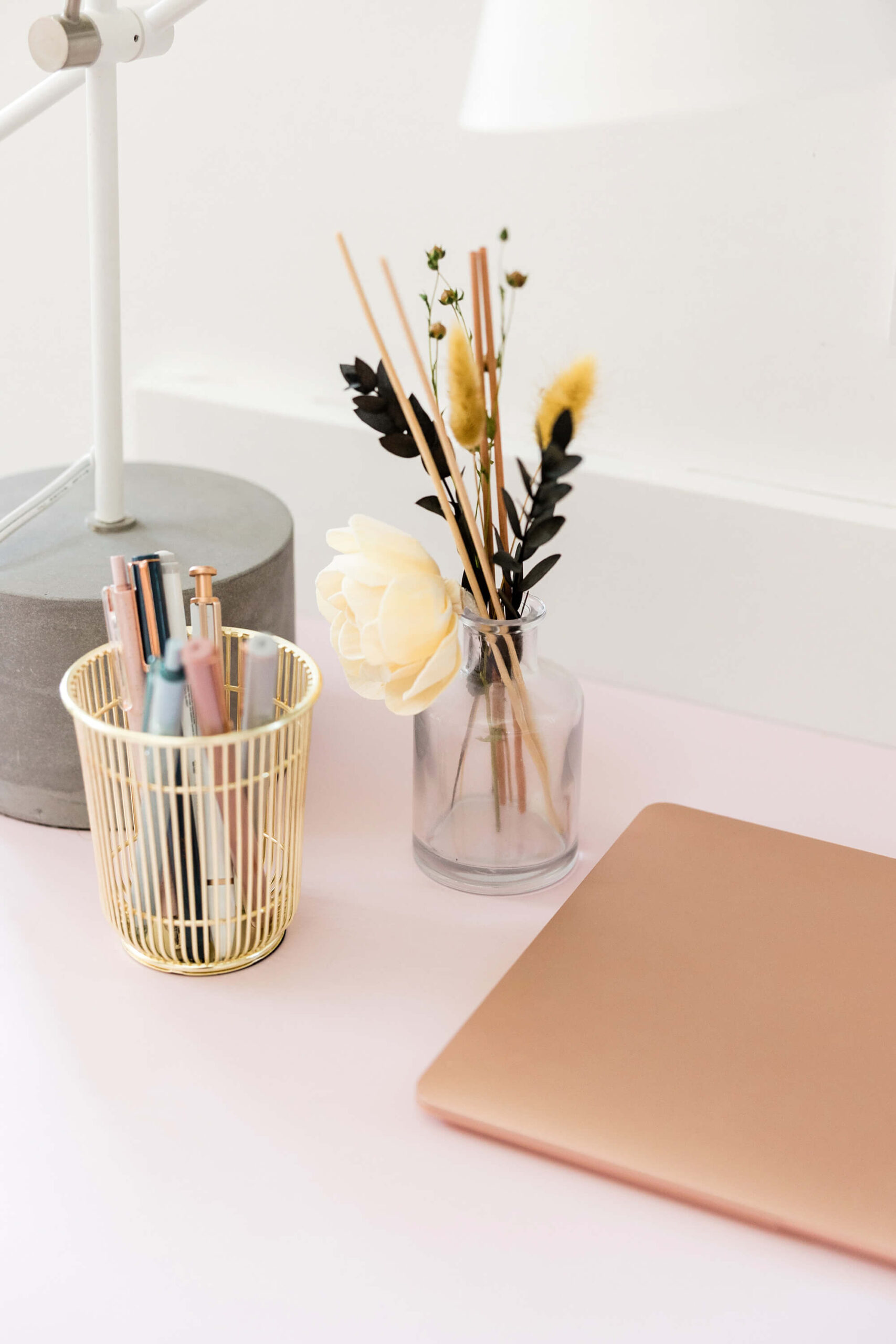 Desk with lamp, pens, flowers, and closed laptop.