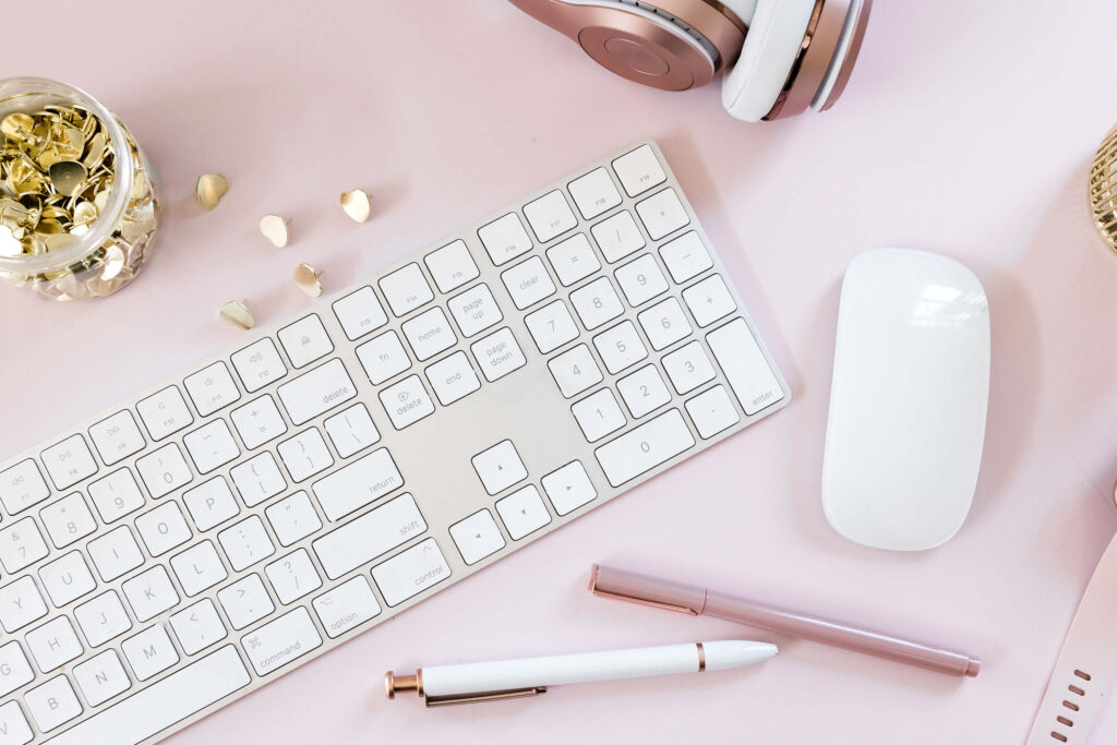 White keyboard, mouse, and pens on pink desk.