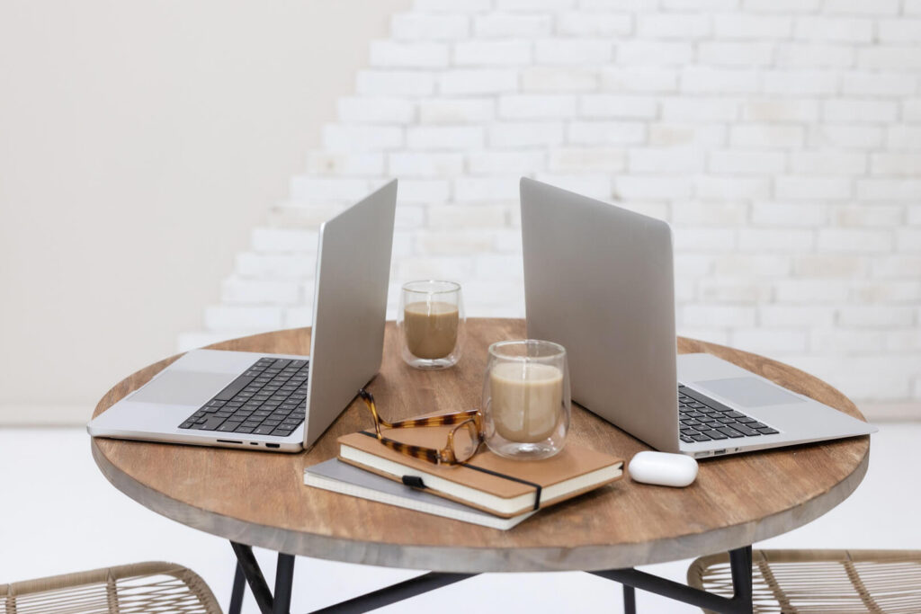 Two laptops on round table with coffee cups.