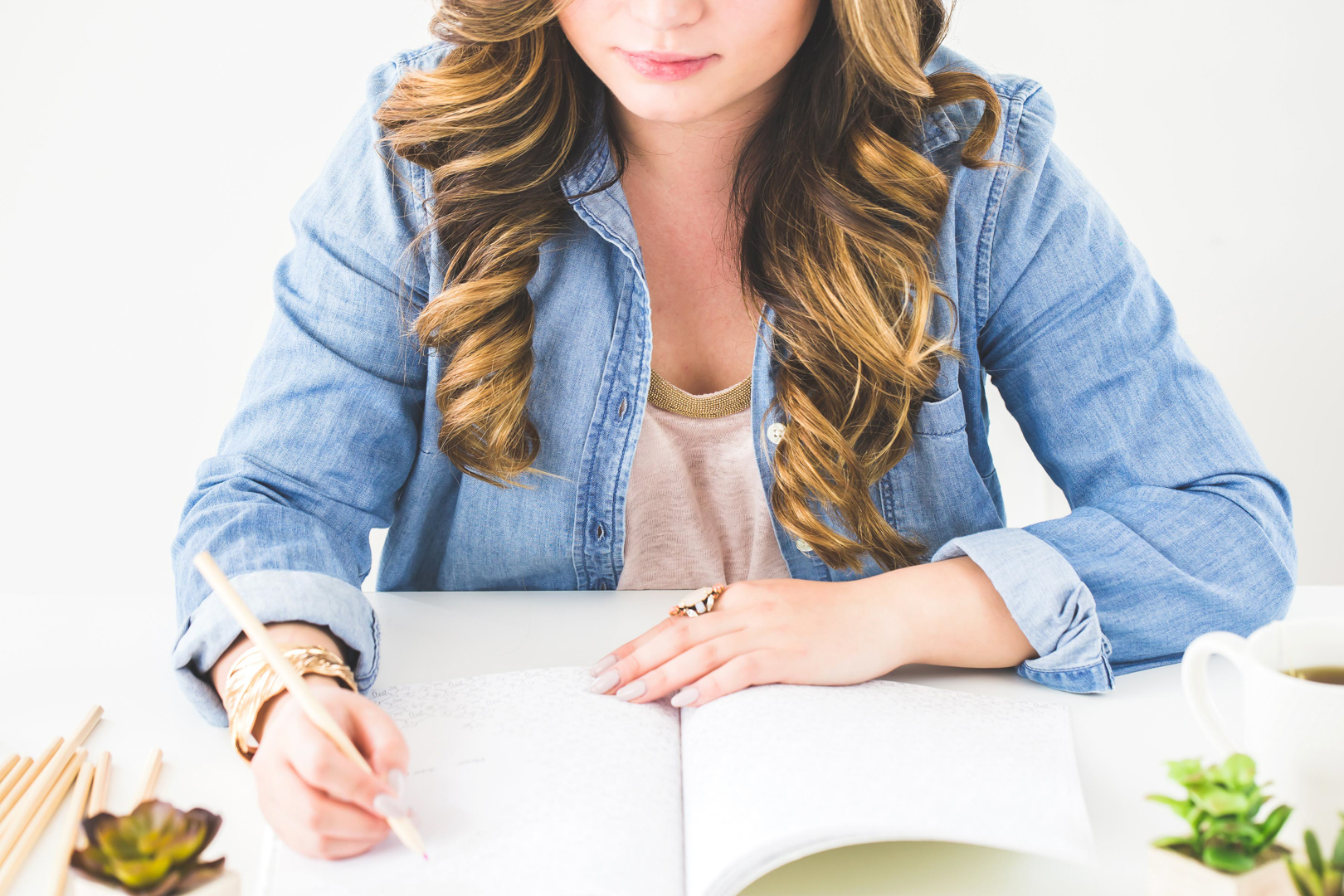 Woman writing in a notebook at white desk.