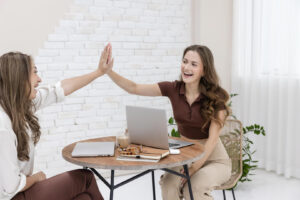 Two women high-fiving at desk with laptops.