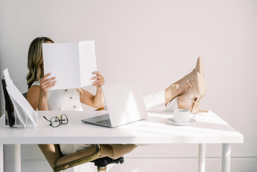 Person relaxing at desk with book and laptop.