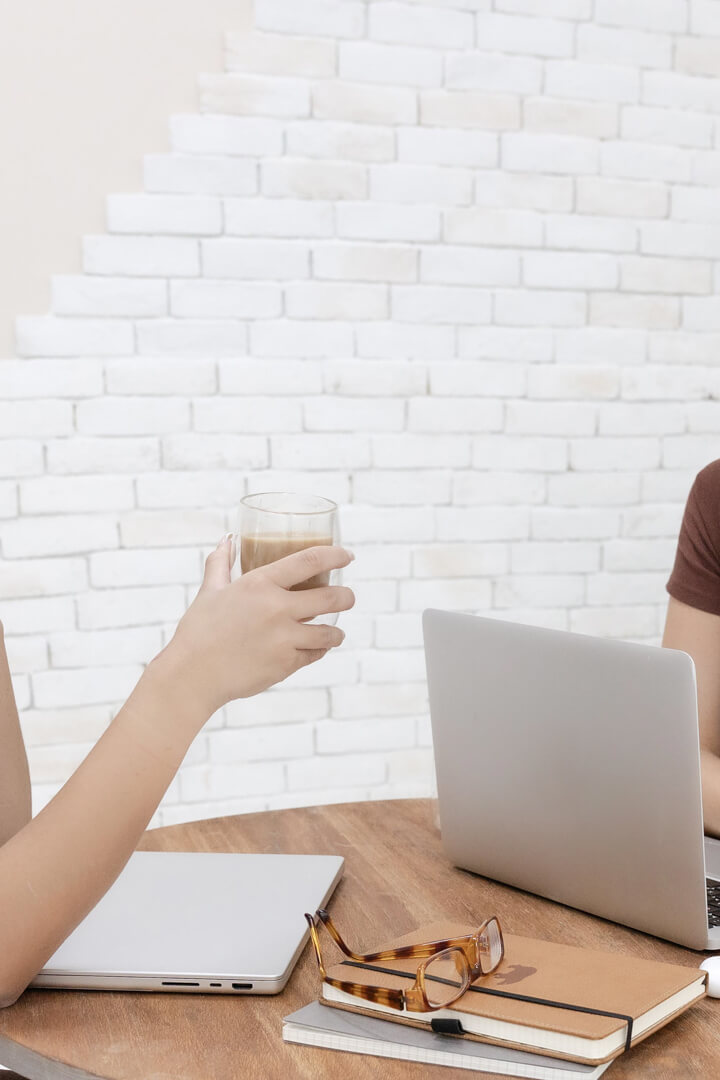 Person holding coffee near laptop and notebooks.