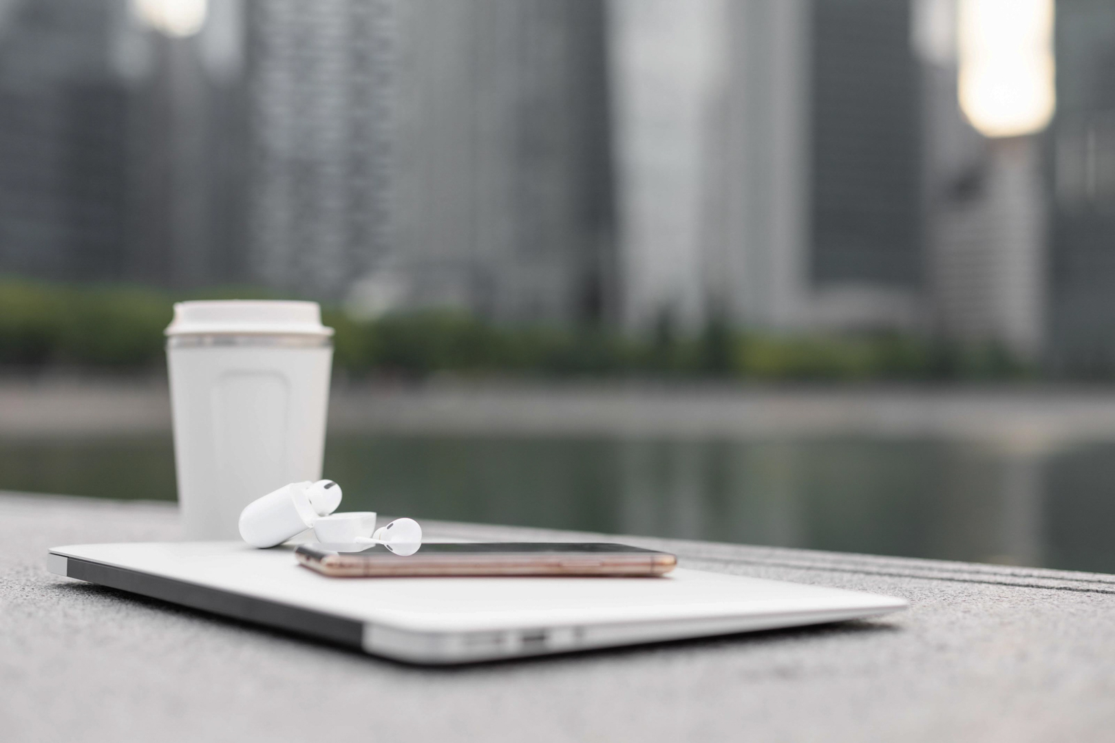 Earbuds, phone, coffee cup on laptop, cityscape background.