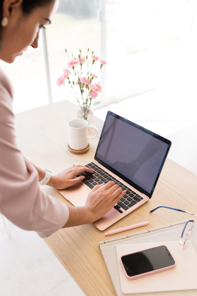Person typing on laptop with flowers nearby.