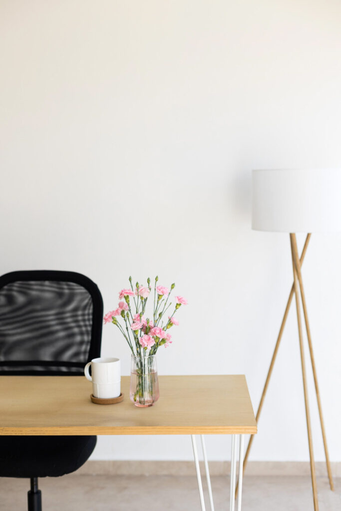 Minimalist desk with flowers, chair, and floor lamp.