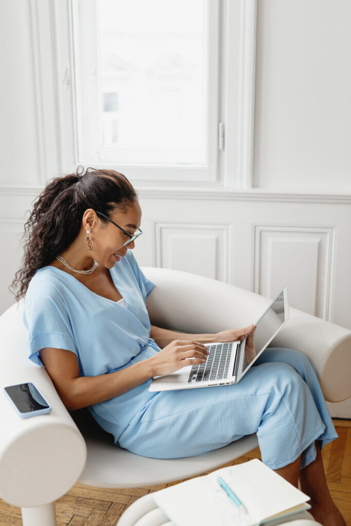 Woman in blue outfit using laptop on couch.