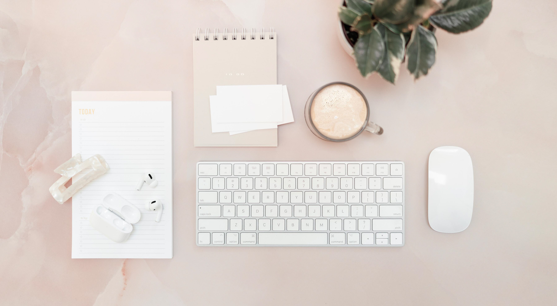 Minimalist desk with keyboard, notebook, coffee, plant.