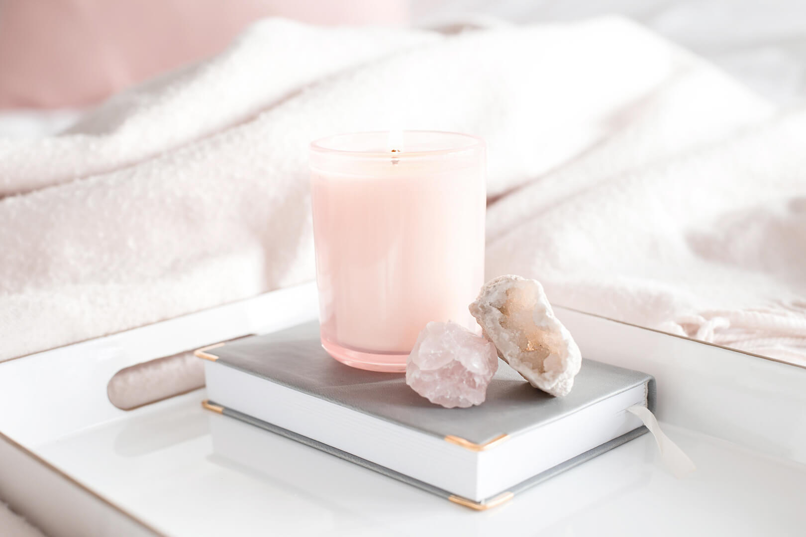 Pink candle with crystals and journal on tray.