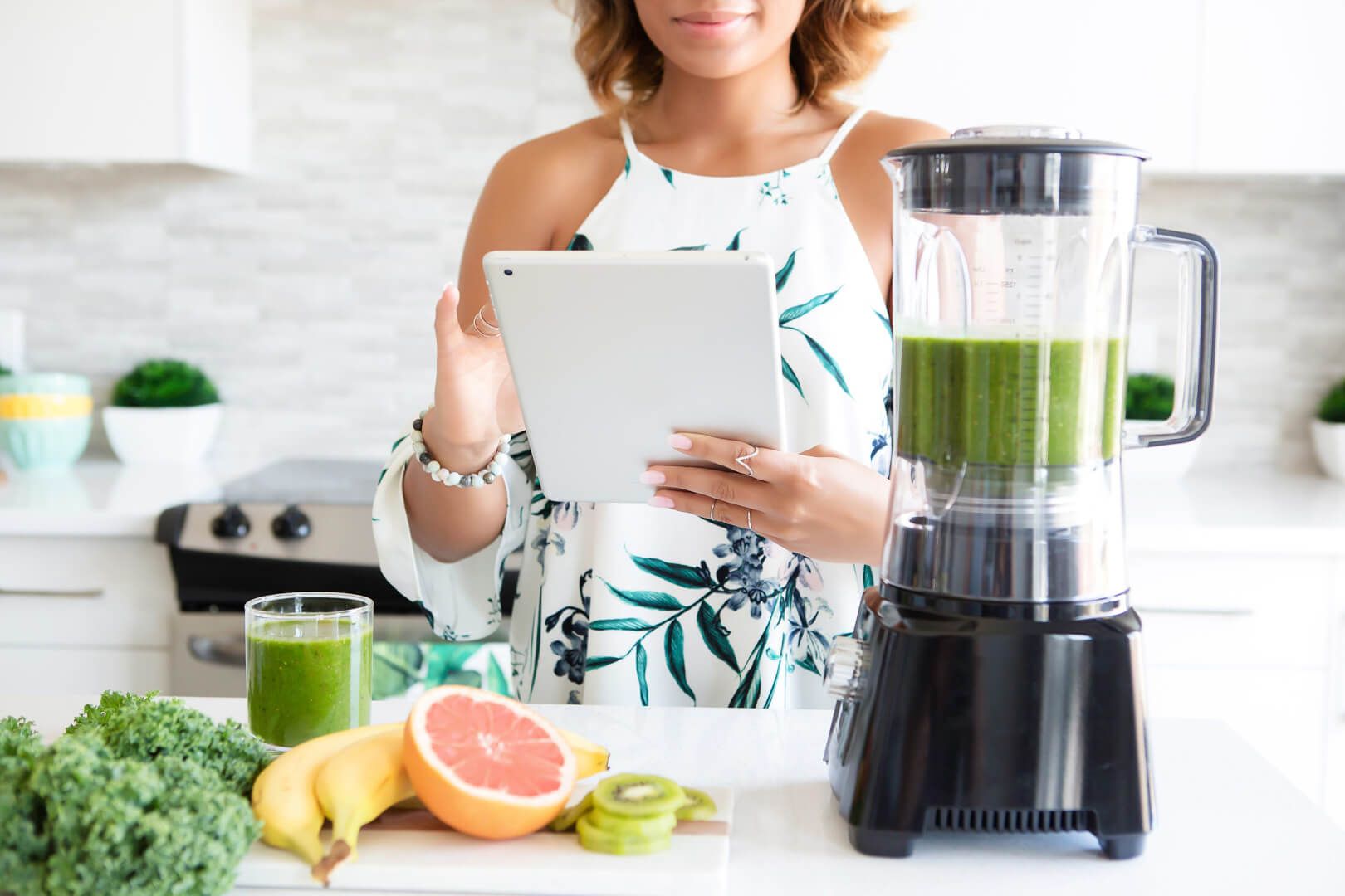 Woman preparing smoothie with tablet in kitchen.