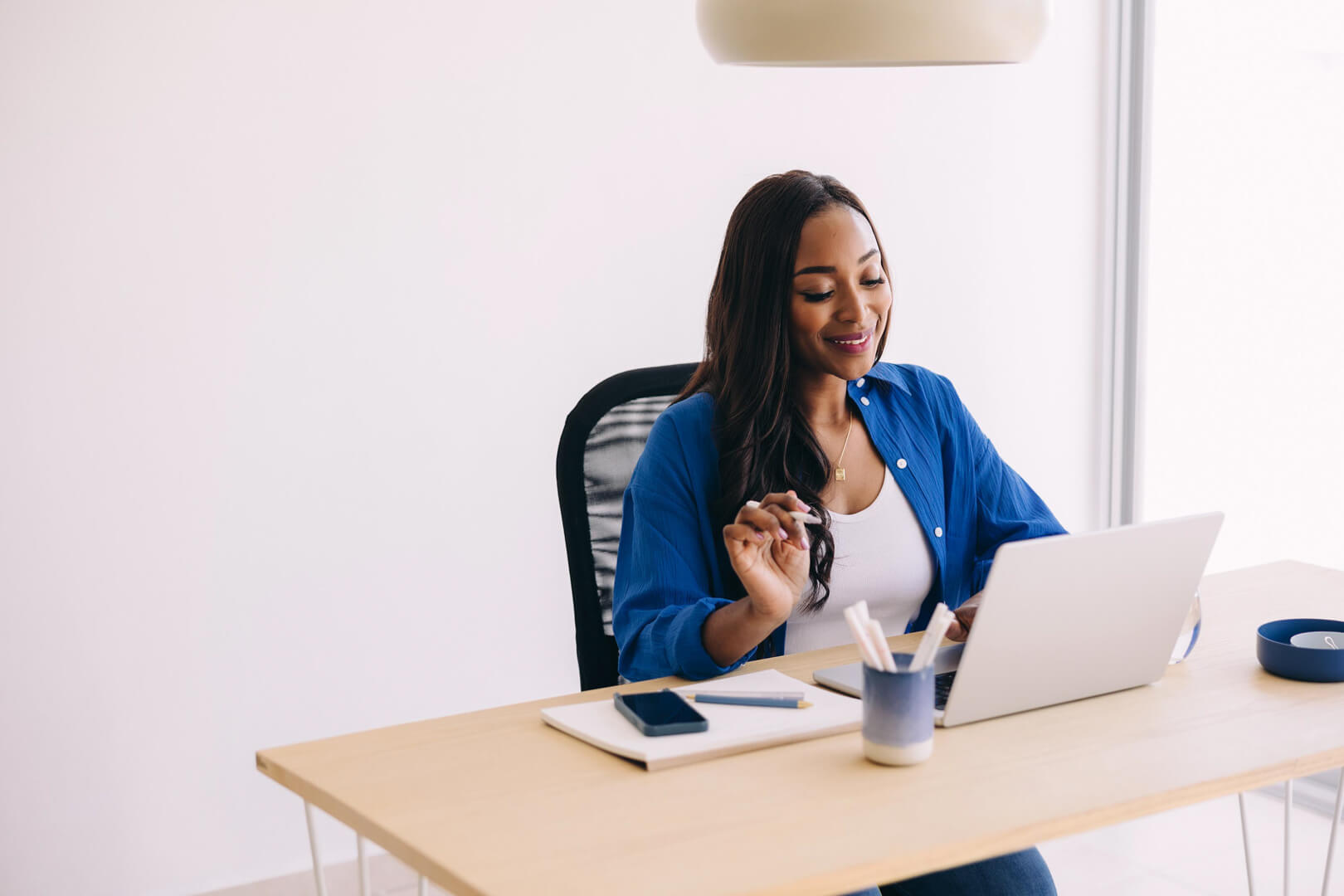 Woman working on laptop at desk, smiling.