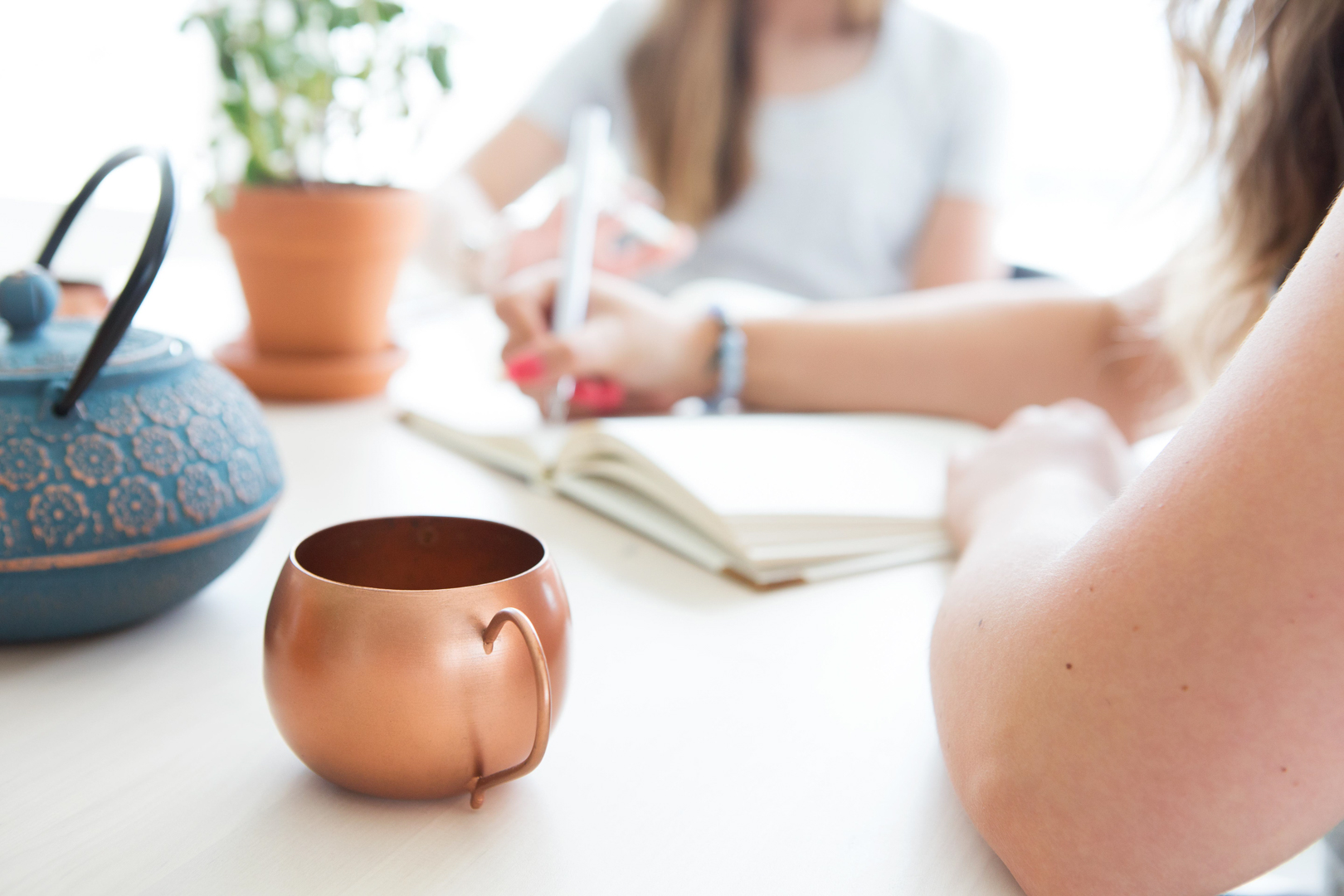 People writing with notebook and copper mug on table.