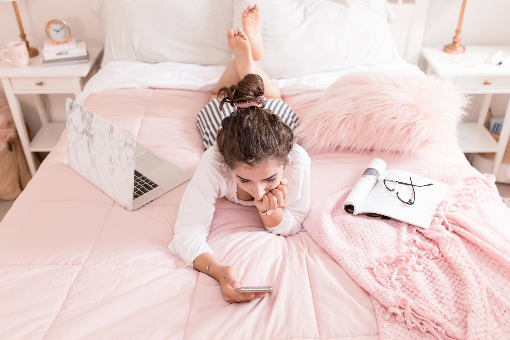 Woman relaxing on bed with laptop and phone.