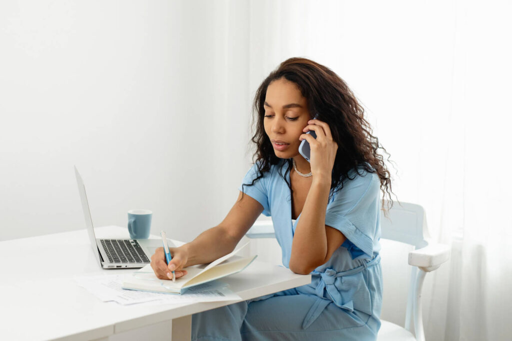 Woman on phone writing at desk.