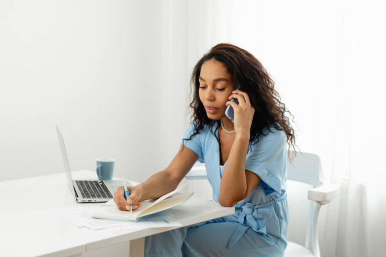 Woman on phone writing at desk.