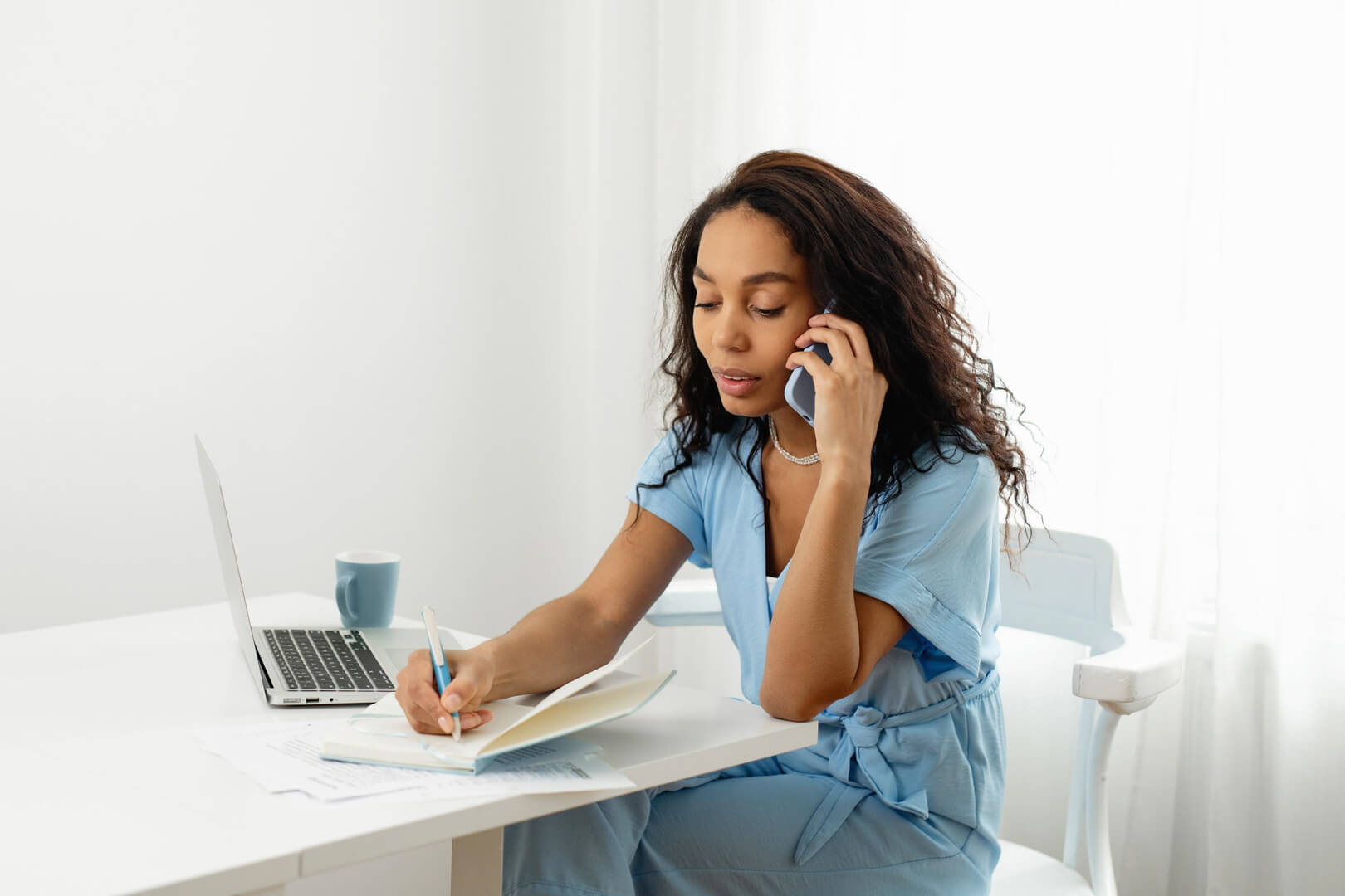 Woman on phone writing at desk.