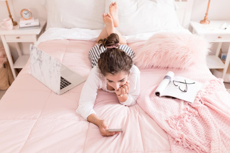 Woman relaxing on bed with laptop and phone.