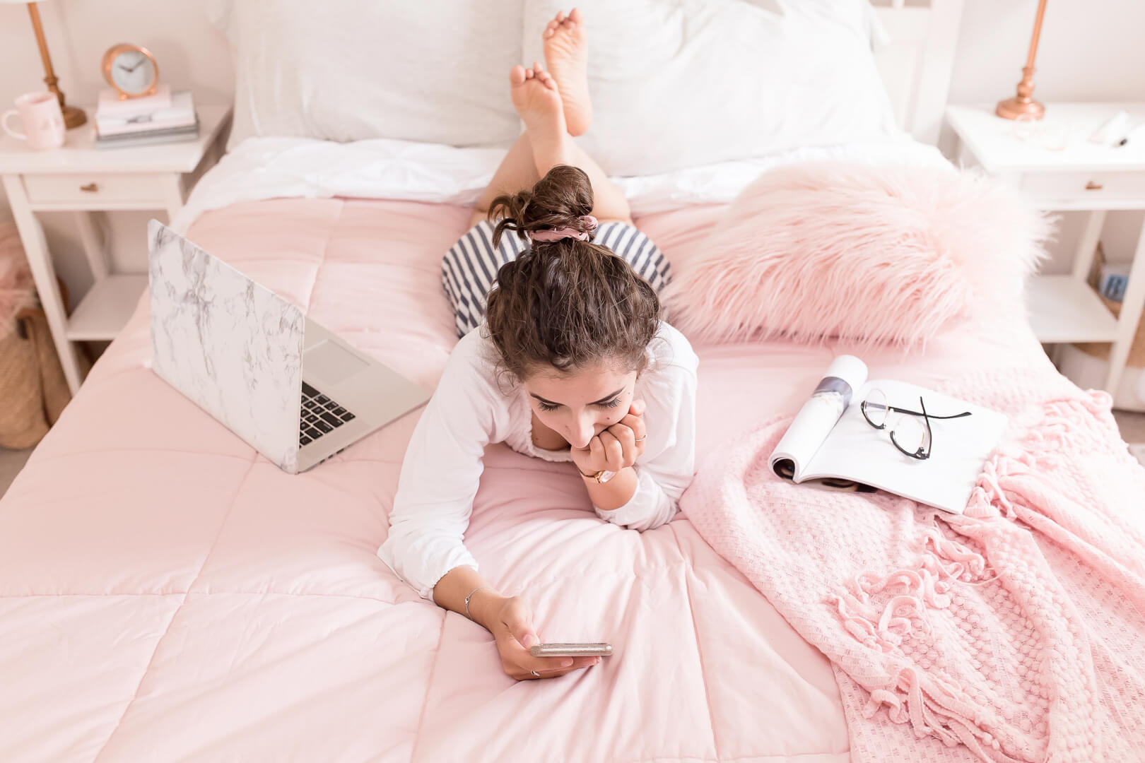 Woman relaxing on bed with laptop and phone.