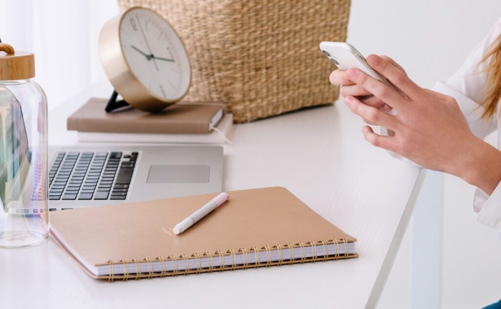 Person using smartphone at a desk with laptop