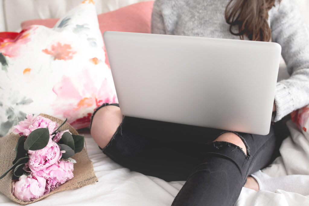 Person with laptop and pink flowers on bed.